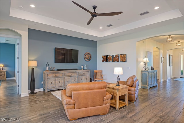 living room featuring arched walkways, a raised ceiling, visible vents, and dark wood-style flooring