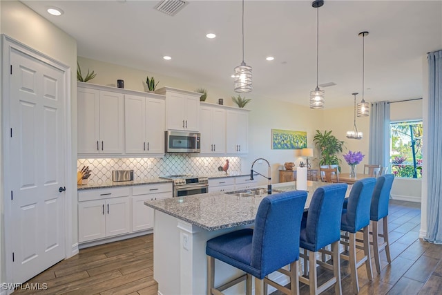 kitchen with stainless steel appliances, a sink, decorative light fixtures, and white cabinets