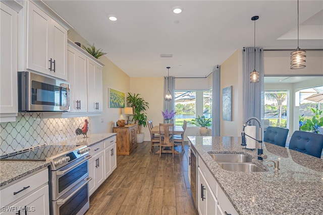 kitchen with decorative light fixtures, appliances with stainless steel finishes, white cabinetry, a sink, and light stone countertops