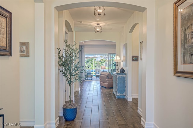 hall with arched walkways, dark wood-style flooring, and baseboards