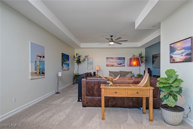 living room featuring carpet floors, a tray ceiling, ceiling fan, and baseboards