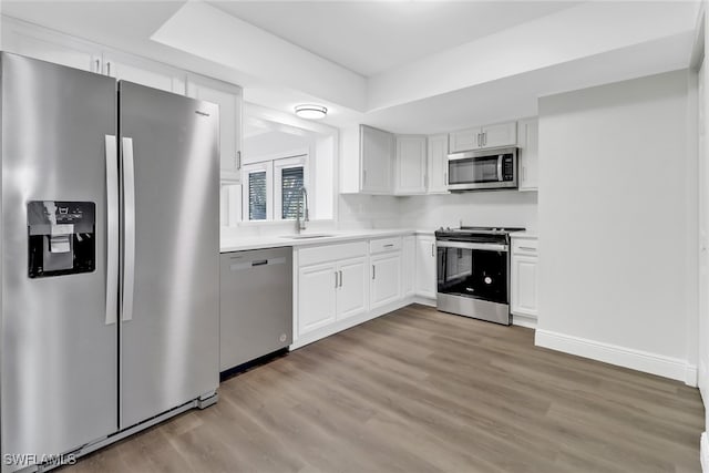 kitchen featuring sink, light hardwood / wood-style flooring, white cabinetry, stainless steel appliances, and a raised ceiling