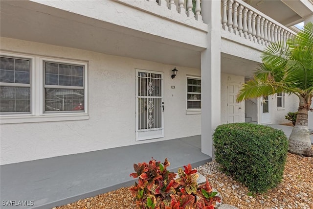 view of exterior entry featuring a balcony and stucco siding