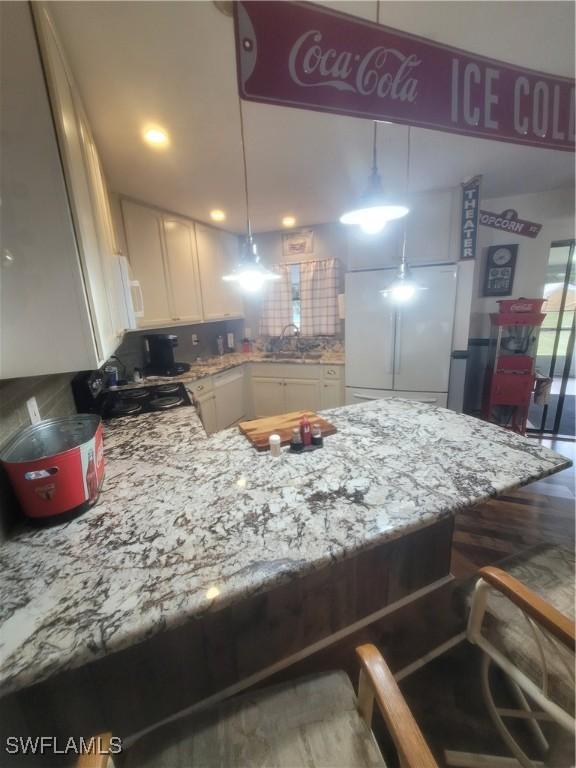 kitchen featuring refrigerator, a breakfast bar area, white cabinets, hanging light fixtures, and kitchen peninsula