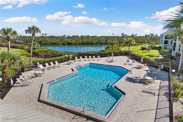 pool with a patio area, a water view, and fence