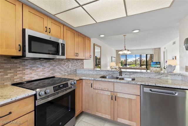 kitchen featuring light stone countertops, stainless steel appliances, a sink, and light brown cabinetry