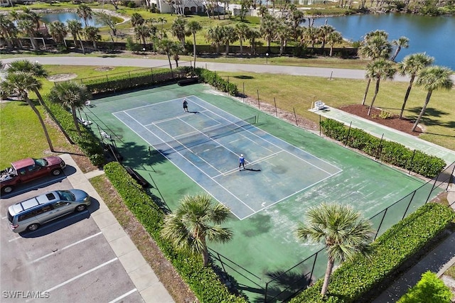 view of tennis court featuring a water view, fence, and a lawn