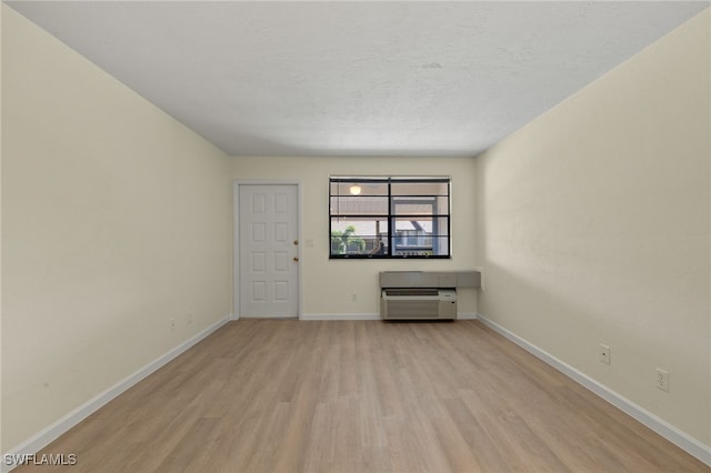empty room featuring a wall mounted air conditioner, a textured ceiling, and light wood-type flooring