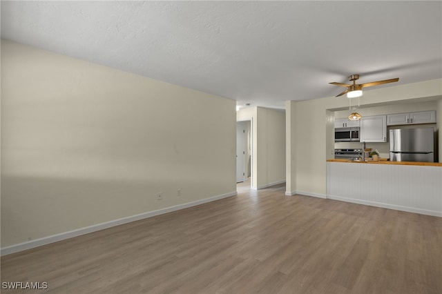 unfurnished living room with ceiling fan, a textured ceiling, and light wood-type flooring