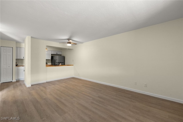 unfurnished living room featuring hardwood / wood-style flooring, ceiling fan, and a textured ceiling