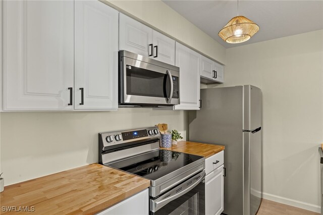 kitchen with stainless steel appliances, white cabinetry, wooden counters, and decorative light fixtures