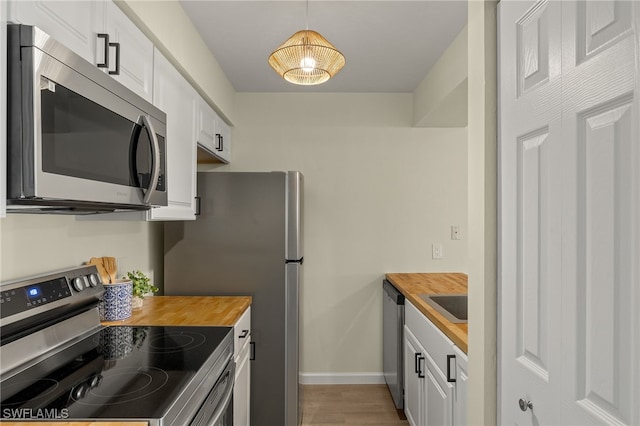 kitchen featuring stainless steel appliances, white cabinetry, hanging light fixtures, and wood counters