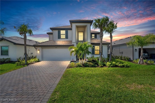 mediterranean / spanish home featuring decorative driveway, an attached garage, a tiled roof, and a front lawn