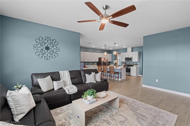 living room featuring light wood-style floors, ceiling fan, and baseboards