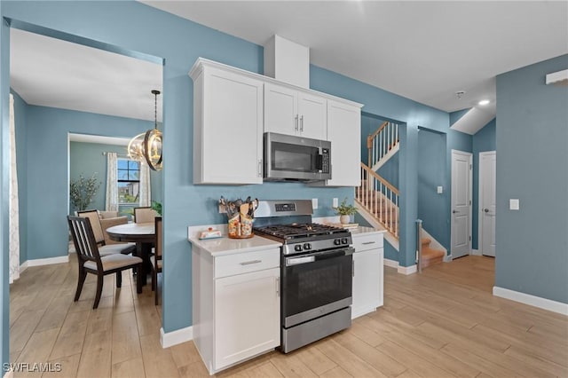 kitchen featuring white cabinets, appliances with stainless steel finishes, light countertops, light wood-style floors, and a notable chandelier