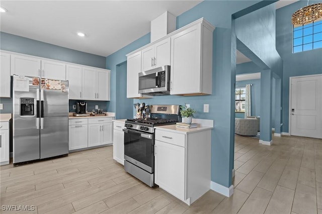 kitchen with baseboards, white cabinets, light wood-style flooring, stainless steel appliances, and light countertops