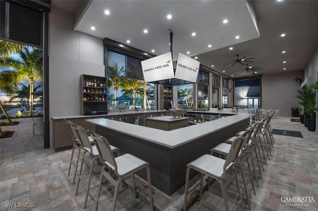 bar featuring ceiling fan, stone finish floor, a community bar, and recessed lighting