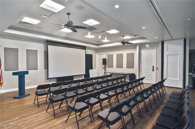 cinema room featuring a tray ceiling, ceiling fan, and hardwood / wood-style flooring