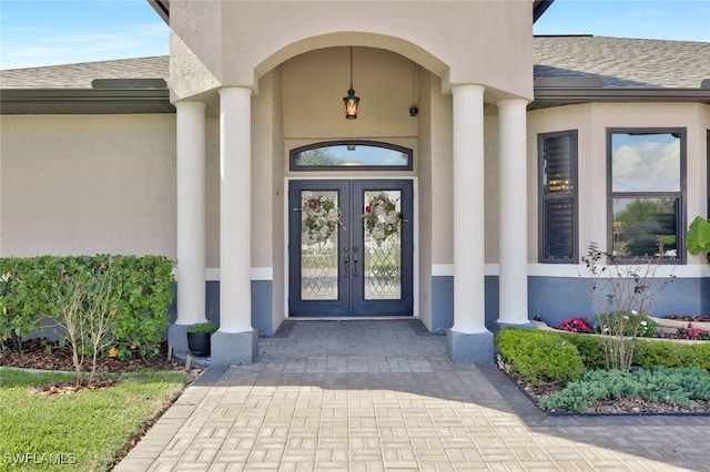 view of exterior entry featuring french doors, roof with shingles, and stucco siding