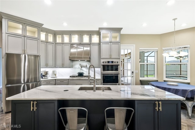 kitchen featuring a large island, appliances with stainless steel finishes, decorative light fixtures, extractor fan, and a sink