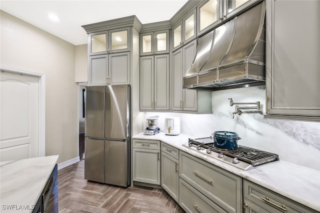 kitchen featuring baseboards, glass insert cabinets, stainless steel appliances, ventilation hood, and recessed lighting