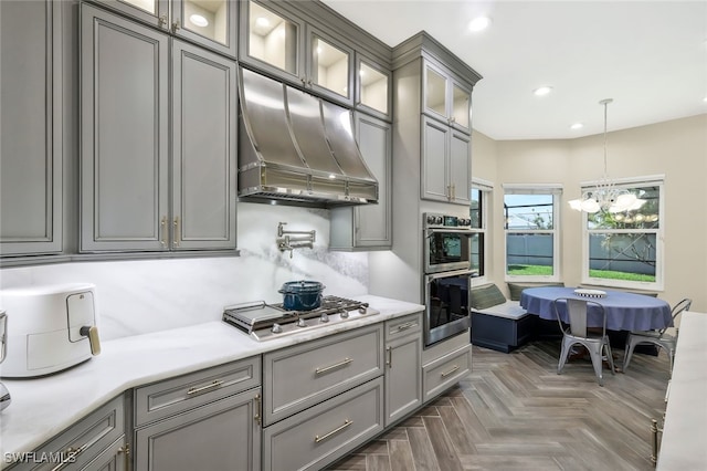 kitchen featuring glass insert cabinets, decorative light fixtures, range hood, light countertops, and stainless steel appliances