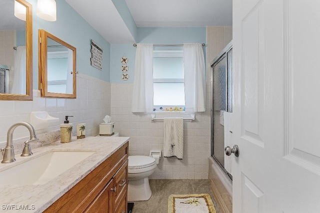 bathroom featuring bath / shower combo with glass door, vanity, toilet, and tile walls