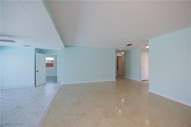 empty room with light speckled floor, visible vents, baseboards, and a ceiling fan