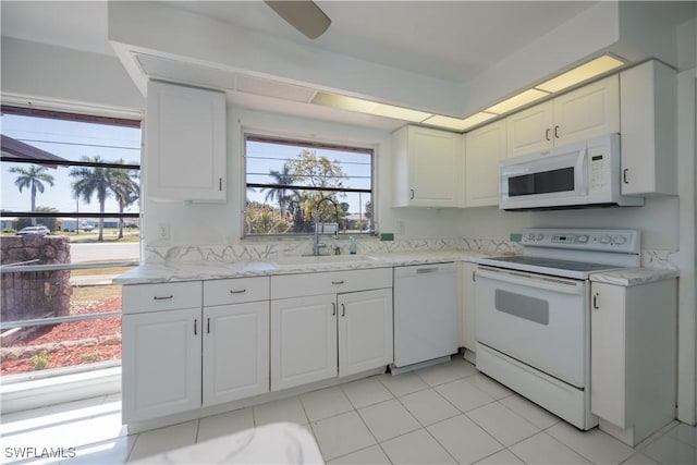 kitchen with light tile patterned floors, white appliances, a sink, white cabinets, and light stone countertops