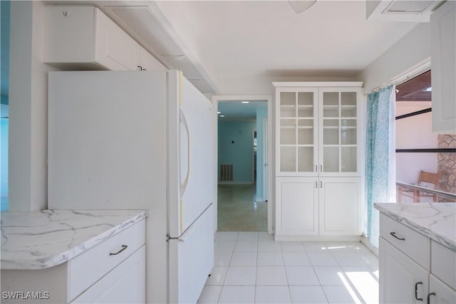 kitchen with visible vents, white cabinetry, freestanding refrigerator, light stone countertops, and glass insert cabinets