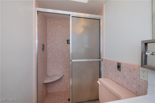 bathroom with toilet, a stall shower, tile walls, and wainscoting