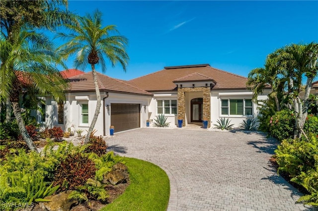 mediterranean / spanish-style house featuring stone siding, a tiled roof, an attached garage, decorative driveway, and stucco siding