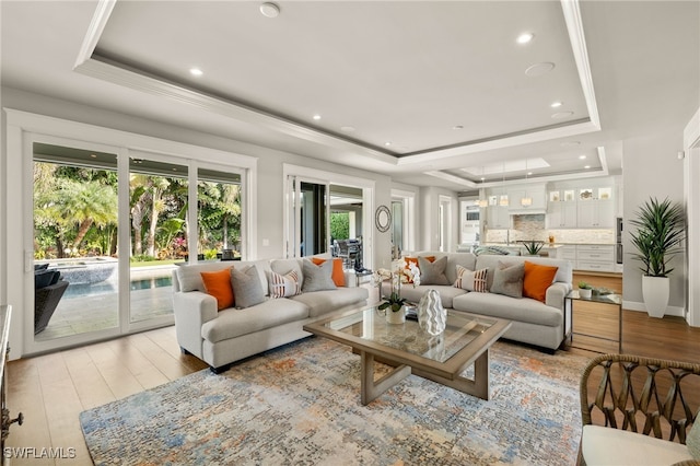 living area with light wood-style flooring, a tray ceiling, crown molding, and recessed lighting