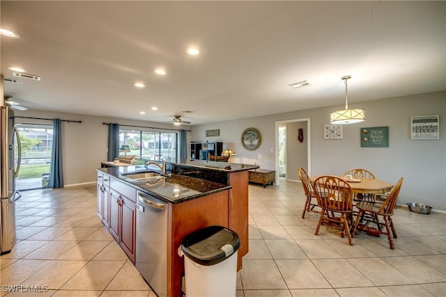 kitchen featuring decorative light fixtures, appliances with stainless steel finishes, a kitchen island with sink, a sink, and dark stone countertops