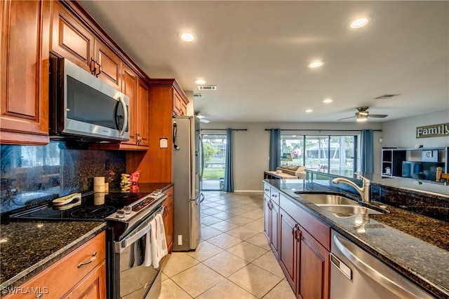 kitchen with dark stone countertops, stainless steel appliances, a sink, and open floor plan