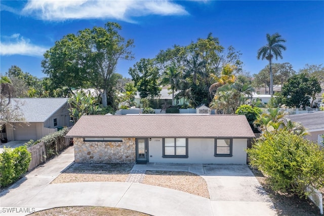 ranch-style home with stone siding, concrete driveway, a shingled roof, and fence