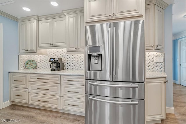 kitchen with light stone countertops, stainless steel refrigerator with ice dispenser, light wood-type flooring, and tasteful backsplash