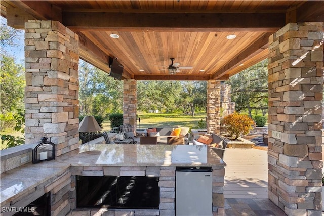 view of patio / terrace with an outdoor kitchen, a wooden deck, ceiling fan, and a bar