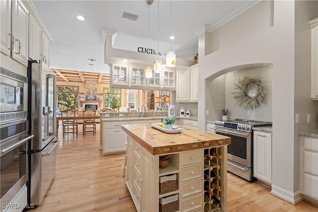 kitchen featuring appliances with stainless steel finishes, a center island, white cabinetry, decorative light fixtures, and butcher block countertops