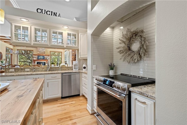 kitchen with butcher block countertops, light hardwood / wood-style flooring, appliances with stainless steel finishes, white cabinets, and decorative backsplash