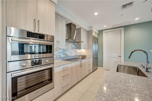 kitchen featuring appliances with stainless steel finishes, sink, wall chimney exhaust hood, light stone countertops, and decorative backsplash