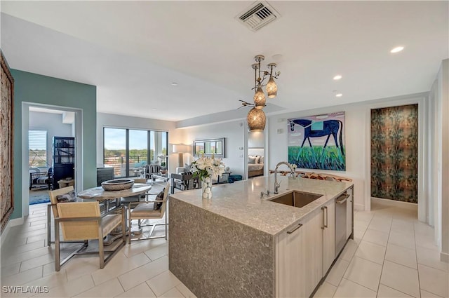 kitchen featuring hanging light fixtures, light stone countertops, light tile patterned flooring, sink, and a kitchen island with sink