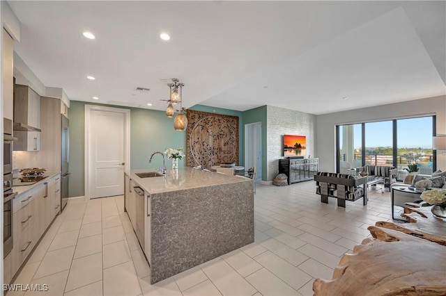 kitchen with a center island with sink, sink, stainless steel appliances, hanging light fixtures, and light stone countertops