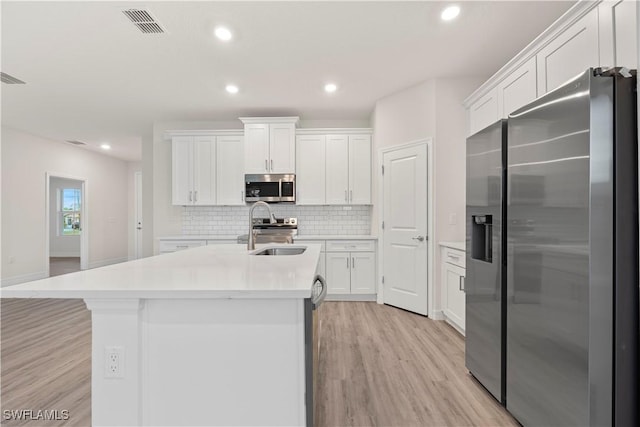 kitchen featuring stainless steel appliances, an island with sink, white cabinets, decorative backsplash, and sink