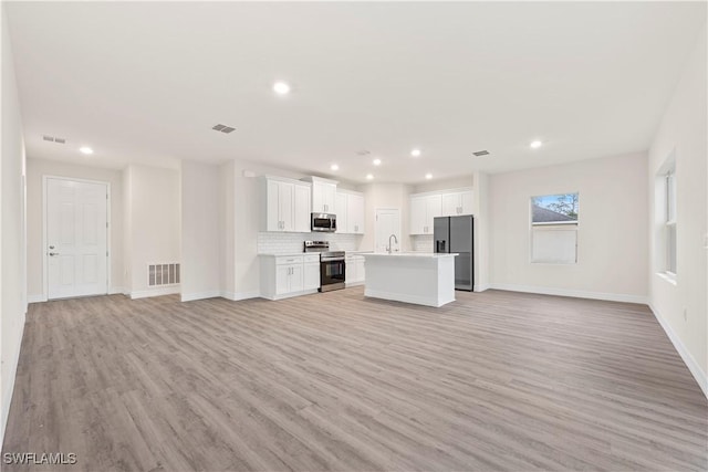 kitchen with white cabinetry, stainless steel appliances, a center island, light hardwood / wood-style floors, and backsplash