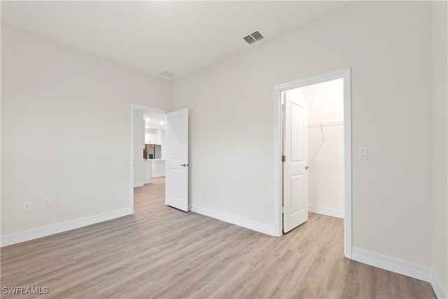 unfurnished bedroom with light hardwood / wood-style flooring, a spacious closet, and a closet