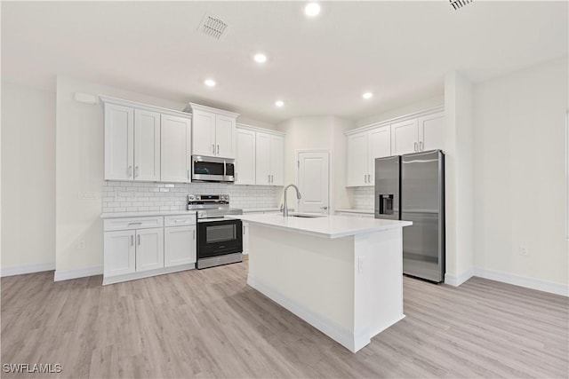 kitchen with light hardwood / wood-style floors, appliances with stainless steel finishes, white cabinetry, and a kitchen island with sink