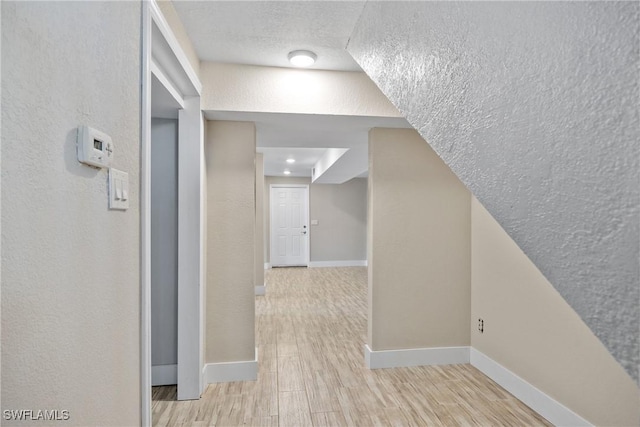 corridor featuring a textured wall, a textured ceiling, baseboards, and wood finished floors