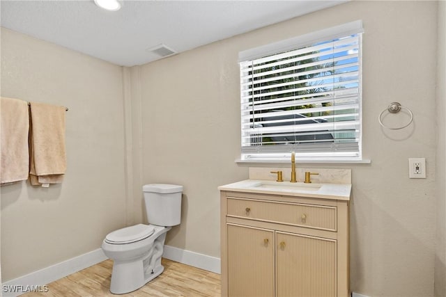 bathroom with visible vents, toilet, vanity, wood finished floors, and baseboards