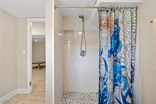 bathroom featuring baseboards, a tile shower, and wood finished floors